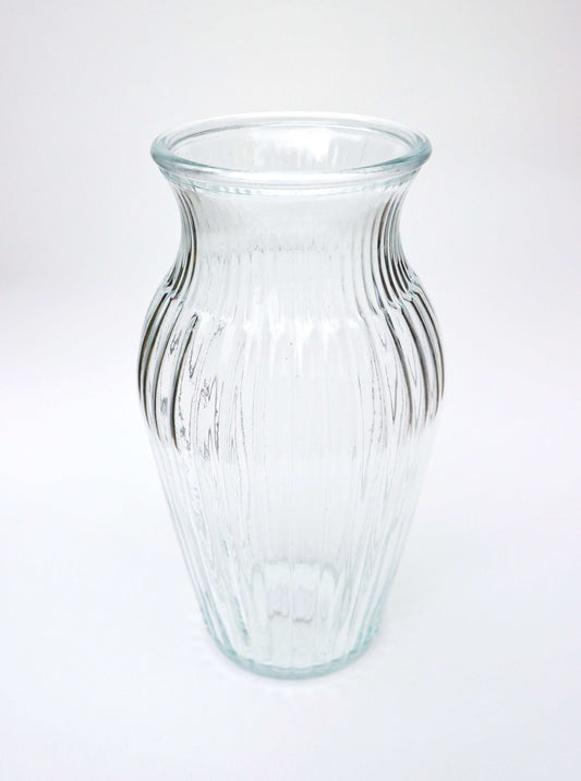 Clear ribbed glass vase with a flared top on a white background.